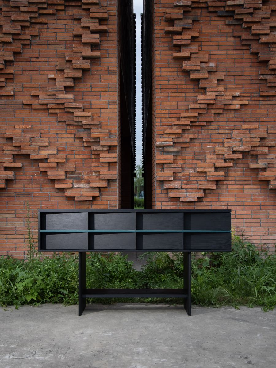 Slit Console in black wood with eight drawers and a thin teal strip, against patterned brick